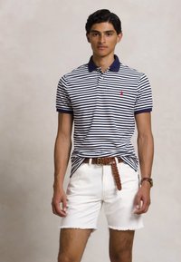 Πόλο μπλούζα λευκής και μπλε ρίγας με γιακά, συνδυασμένη με λευκά τζιν σορτς. Διαθέτει μικρό κόκκινο λογότυπο και καφέ πλεγμένη ζώνη.