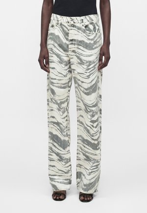 Personne portant un jean taille haute, coupe large avec un imprimé zèbre abstrait gris et blanc, associé à des sandales noires et un haut noir.