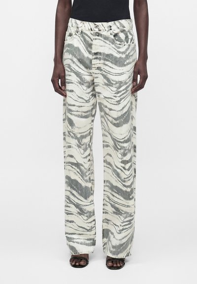 Personne portant un jean taille haute, coupe large avec un imprimé zèbre abstrait gris et blanc, associé à des sandales noires et un haut noir.