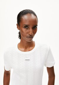 Camiseta de manga corta blanca, hecha de tela acanalada, con cuello redondo y una pequeña etiqueta en el pecho, con una sutil textura lineal.