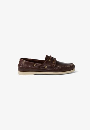 Zapato náutico para hombre de cuero marrón con costuras de mocasín, detalles de cordones, ojales de latón y suela de goma blanca, mostrado en vista lateral.