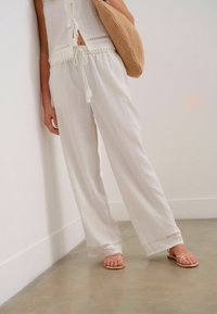 Des pantalons larges en lin blanc avec une taille à cordon de serrage agrémentée de pampilles et un subtil détail brodé à l'ourlet. Associés à des sandales nude.