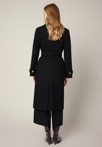 Czarny wełniany płaszcz z paskiem w talii, szerokimi klapami i złotymi guzikami. Charakteryzuje się długim krojem i zróżnicowaną konstrukcją.