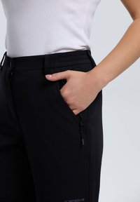 Czarne legginsy z dopasowanym w pasie, bocznymi kieszeniami na zamek i miękką fakturą. Szczegóły przeszyć podkreślają sylwetkę.