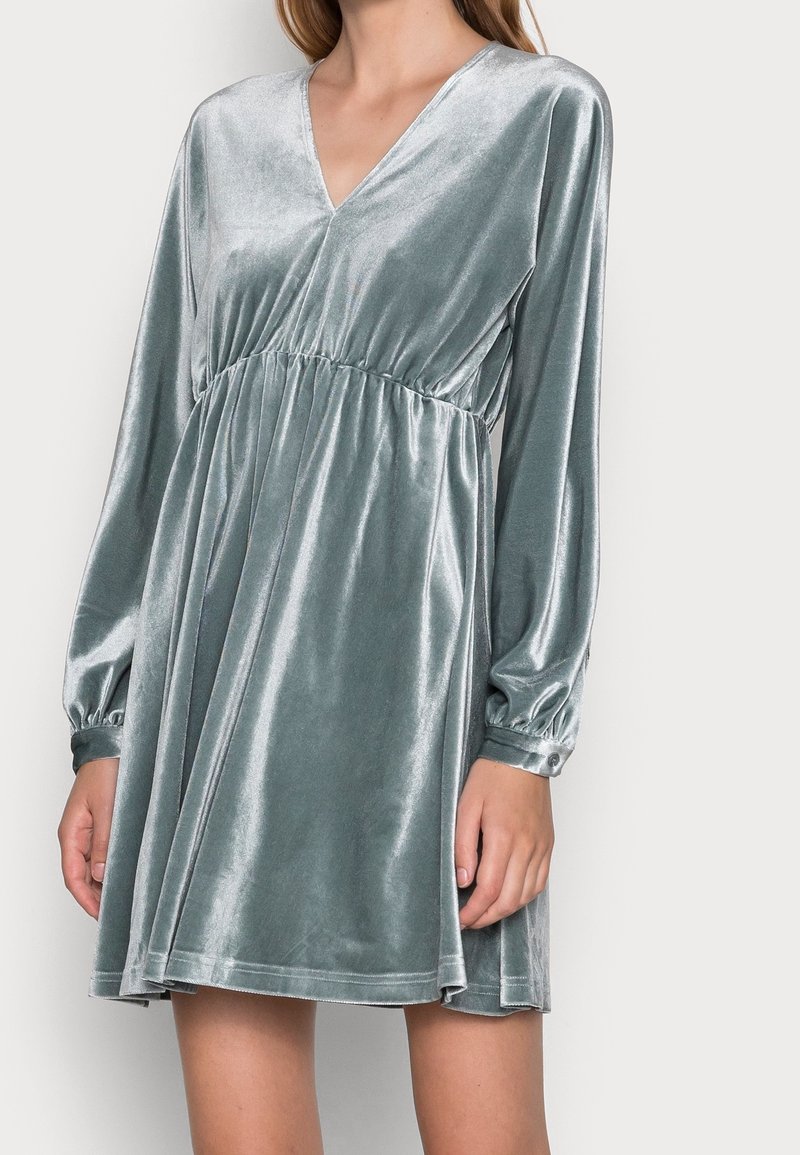 Robe en velours à manches longues de couleur bleu-vert atténuée. Présente un décolleté en V, une taille froncée et une jupe fluide avec des poignets élastiqués. Texture lisse.