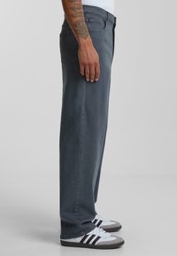 Grijze straight-leg jeans van denim, met een rits, voorzakken en een klassieke pasvorm. Draagt met grijze en witte sneakers.