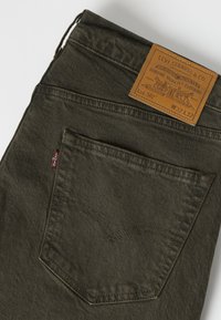 Σκούρο πράσινο πίσω τσεπάκι τζιν Levi's με δερμάτινη ετικέτα μάρκας που δείχνει μέγεθος W32 L32 και κόκκινη ετικέτα Levi’s στη ραφή της τσέπης.