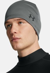 Gray beanie made of stretchy fabric, featuring flat seams and a small black logo on the side; snug fit around the head.