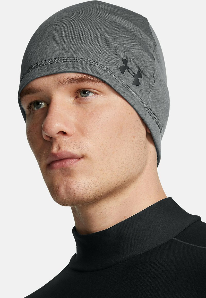 Gray beanie made of stretchy fabric, featuring flat seams and a small black logo on the side; snug fit around the head.