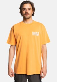Orange cotton t-shirt featuring a crew neckline, short sleeves, and a white graphic print, with a relaxed fit and a smooth texture.