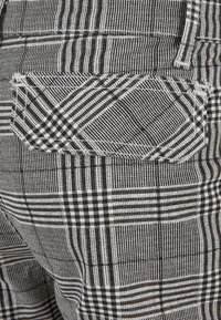 Tissu à carreaux noir et blanc avec des motifs géométriques cousus dans une poche arrière d’un vêtement.