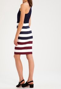 Marinblå topp med en enda axelrem; randig pennkjol i vitt, mörkblått och bordeaux. Svarta klacksandaler fulländar looken.