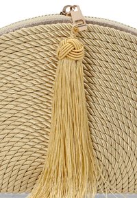 Bolso de mano tejido en oro con una superficie texturizada, que presenta un pompón decorativo y un cierre de cremallera metálica.
