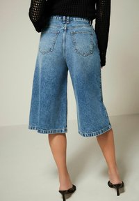Culotte in denim blu con una vestibilità rilassata, vita a media altezza e tasche, caratterizzati da un lavaggio chiaro e dettagli sfilacciati all'orlo.
