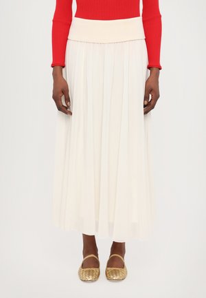 White pleated maxi skirt with a wide cream waistband, paired with gold woven flats. The top is a fitted red long-sleeve ribbed sweater.