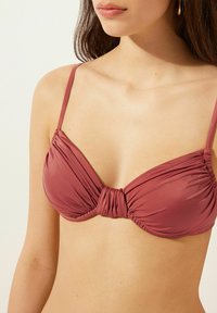 Rosa bikinitopp med mjukt, hopdraget tyg, justerbara band och en vriden detalj i mitten. Slät textur med en minimalistisk design.