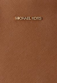 Καφέ υλικό με υφή, με χρυσό λογότυπο "MICHAEL KORS". Απλός σχεδιασμός με λεία επιφάνεια και διακριτική υφασμένη λεπτομέρεια.