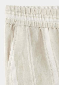 Primer plano de una cintura elástica beige con franjas blancas verticales texturizadas en una prenda de tela ligera.