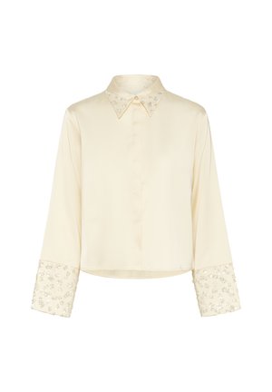 Chemise crème à manches longues avec un col, poignets floraux ornés, texture satin lisse et design lég�èrement court.