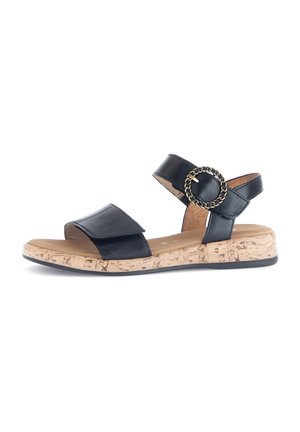 Black leather sandal with adjustable straps, cork-style wedge sole, and gold chain accent, featuring a flat black outsole.