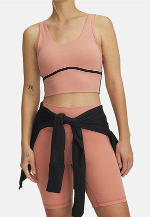 Kvinde iført en lyserød sports-bh og matchende højtaljede cykelshorts med en sort langærmet top bundet om livet.