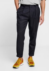 Marinblå randiga byxor med lös passform, med framfåll, sidofickor och uppvikta fållar, i kombination med färgglada sneakers.