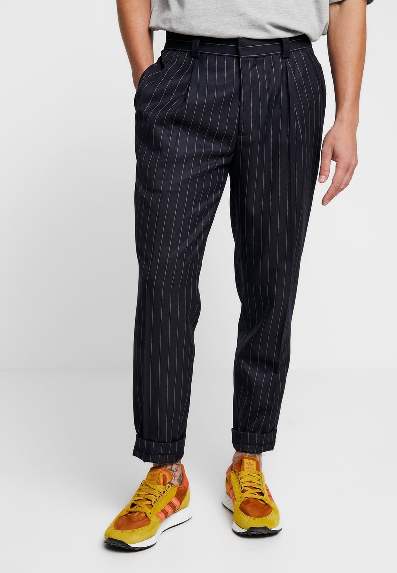 Marinblå randiga byxor med lös passform, med framfåll, sidofickor och uppvikta fållar, i kombination med färgglada sneakers.