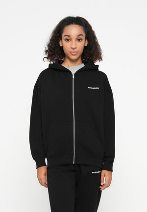 Black zip-up hoodie with a front pocket and ribbed cuffs. Features a silver logo on the left chest. Paired with matching black sweatpants.