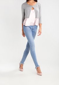 Grå kort cardigan med rund hals, lagd över en ljusrosa satintopp. Ljusblå skinny jeans med trasiga nederkanter, tillsammans med rosa klackar.