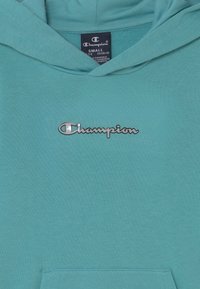 Felpa turchese realizzata in misto cotone, presenta una tasca a marsupio e un logo Champion cucito in argento sul petto. Taglia: Small.
