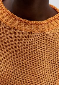 Oranger Strickpullover mit einer lockeren, offenen Maschenstruktur und geripptem Ausschnitt, der ein lässiges Design und atmungsaktiven Stoff präsentiert.