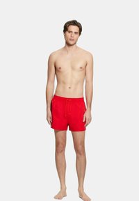 Pantaloni da bagno rossi realizzati in materiale leggero, con vita elastica, cordino e tasche laterali. Corti e dalla texture liscia.