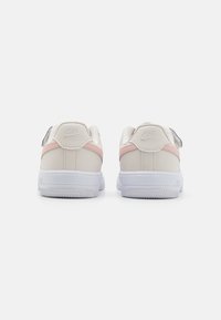 Nike tenisice u boji off-white i pastelno ružičastoj, s glatkim kožnim gornjim dijelom, podstavljenim ovratnikom i bijelim gumenim potplatom s teksturiranim detaljima.