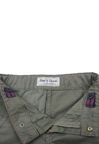 Gröna bomullsshorts för barn med en strukturerad yta, röda sömmar och detaljaccent. Har en ficka med dragkedja och ett varumärkesmärke.