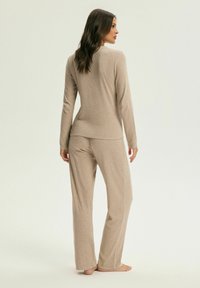 Beżowy zestaw odzieży wypoczynkowej z długimi rękawami i długimi spodniami. Miękka, teksturowana tkanina, luźny krój i okrągły dekolt. Brak widocznych wzorów lub okuć.