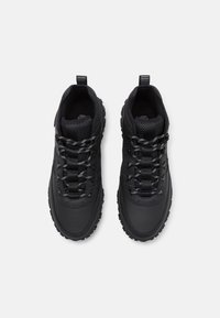 Black outdoor shoes feature a textured upper with a smooth finish, round laces, cushioned collar, and rugged rubber soles for grip.