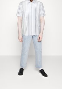 Camicia a righe a maniche corte di colore azzurro chiaro e bianco, abbinata a jeans in denim azzurro chiaro e scarpe da ginnastica nere con suole bianche.