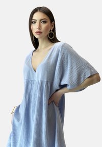 Vestido azul claro, texturizado, con escote en V y mangas cortas, que presenta un corte holgado y una cintura fruncida para una silueta relajada.