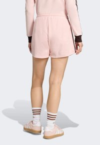 Ružové flísové šortky s elastickým pásom, s jemnou textúrou. Nosené s bielymi ponožkami a ružovými topánkami s hnedými pruhmi.