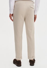 Beżowe lniane spodnie o prostym kroju, z jedną kieszenią z tyłu i podwiniętymi mankietami, w zestawie z brązowymi butami.