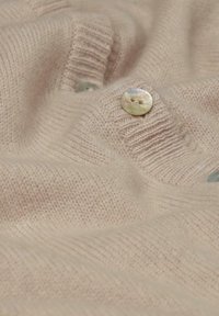 Beige gestrickter Pullover mit einer weichen Textur, der zwei runde, hellfarbige Knöpfe und Rippendetails entlang der Kanten aufweist.