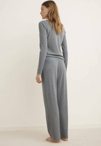 Šedý loungewear set s dlouhým rukávem a širokými kalhotami, vyrobený z měkké látky s hladkou strukturou. Výrazný minimalistický design.