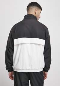 Giacca a vento color block bianco e nero con colletto alto, polsini elasticizzati e orlo arricciato. Tessuto testurizzato con un design leggero.