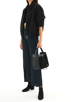 Black cropped bomber jacket with a smooth texture, high-waisted dark denim jeans, and a black bucket bag with a patterned finish.