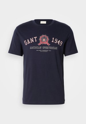 T-shirt in cotone navy a maniche corte con colletto rotondo, caratterizzato da testo bianco e rosso e un logo circolare con "GANT," "1949," e "AMERICAN SPORTSWEAR."