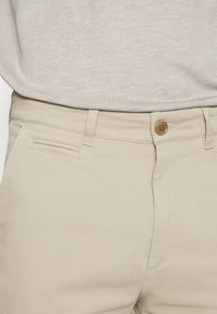 Beiga bomull byxor med framfickor och knappstängning. Har en slät yta och subtila sömdetaljer längs sömmarna.