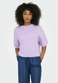 Lilac krāsas, īsām piedurknēm adīta džemperis ar ribotām tekstūrām un apaļu dekoltē, apvienots ar brīvām, tumši zilām biksēm, bez redzamām rakstām.