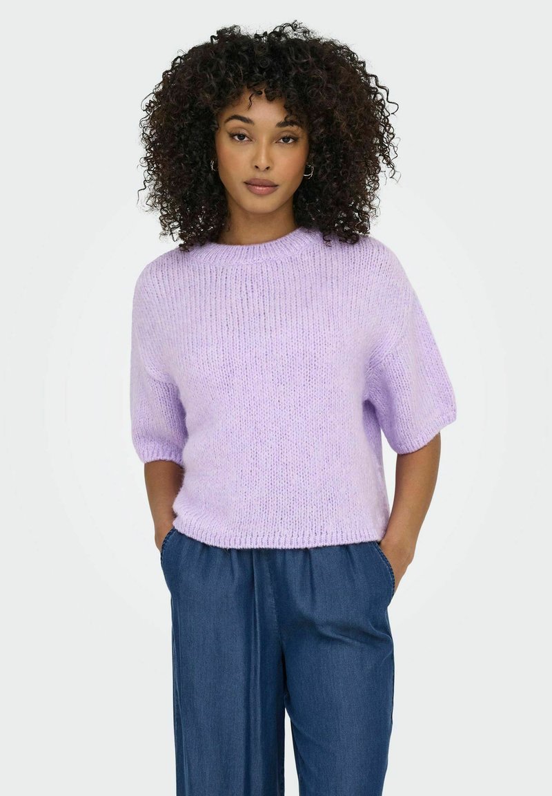 Lilac krāsas, īsām piedurknēm adīta džemperis ar ribotām tekstūrām un apaļu dekoltē, apvienots ar brīvām, tumši zilām biksēm, bez redzamām rakstām.