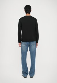 Μαύρη φούτερ μπλούζα με στρογγυλή λαιμόκοψη και μακριά μανίκια, γεμάτη με ανοιχτό μπλε τζιν που τελειώνει σε φλάρε και έχει φθαρμένη υφή denim.