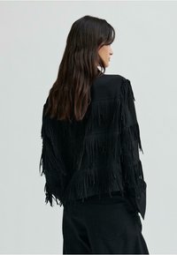 Čierna friganá bunda vyrobená z jemného materiálu, s vrstvenými strapcami na rukávoch a chrbte, klasickým golierom a zapínaním na gombík.